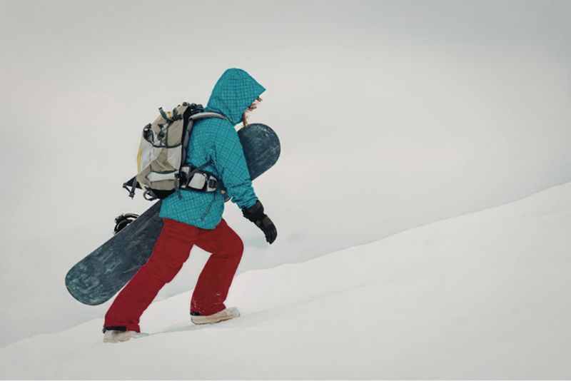 Snowboarder with gear climbing mountain